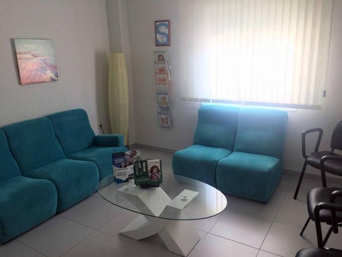 Una sala de estar con muebles azules y una mesa de centro de cristal.