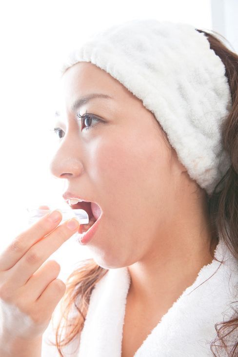 Una mujer que lleva una diadema blanca se cepilla los dientes.