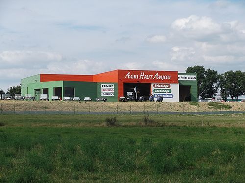 Bâtiment vert et orange avec l'inscription « Acti Haut Anjou » sur la façade, situé dans un champ.