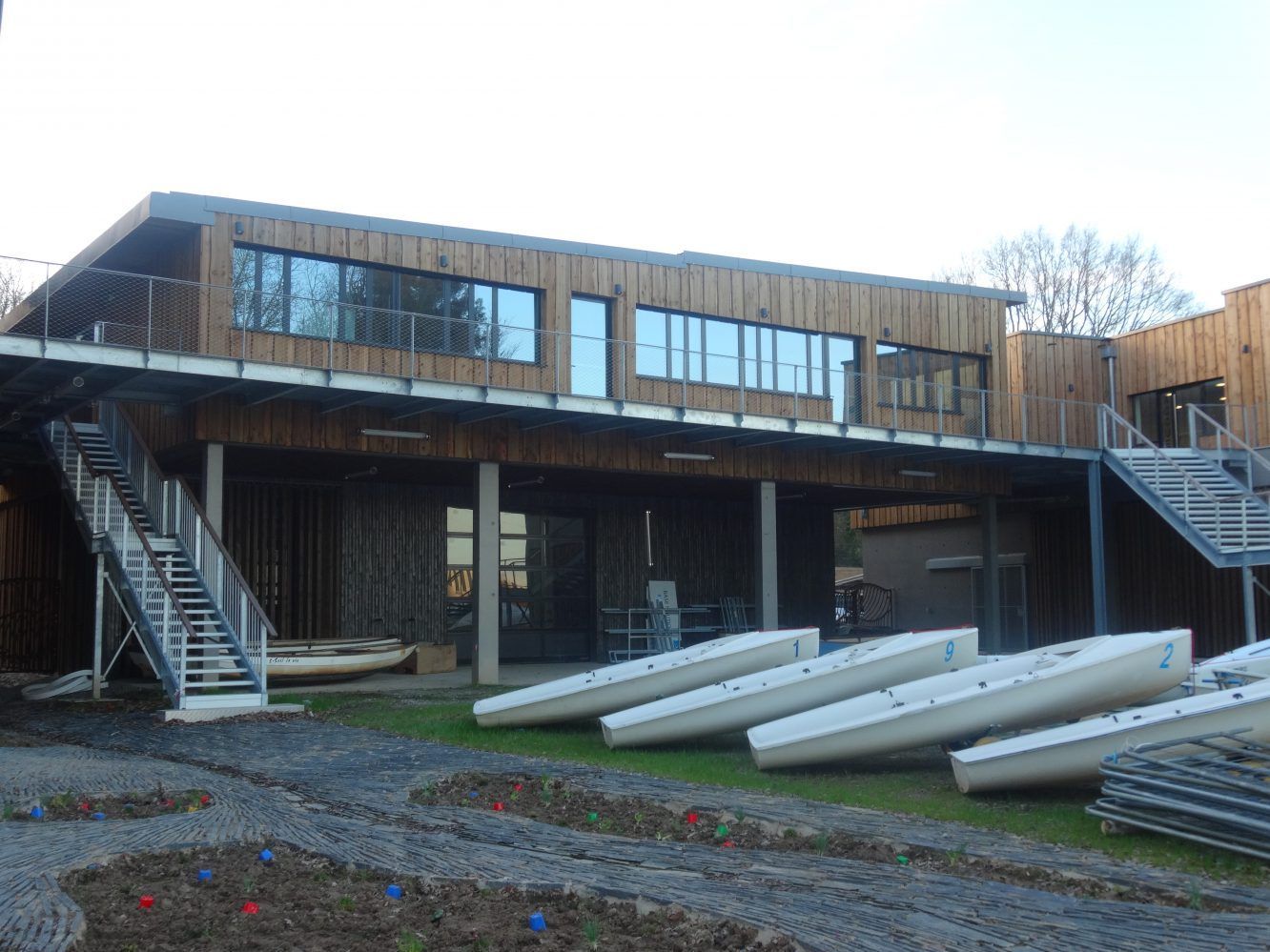 Hangar à bateaux avec plusieurs bateaux blancs alignés sur l'herbe. Extérieur en bois, ciel bleu.