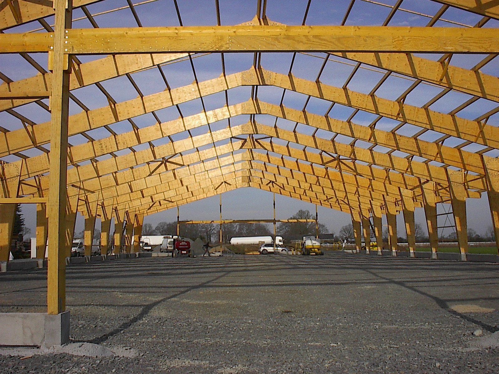 Bâtiment à ossature bois en construction ; vue intérieure des poutres et des chevrons sur fond de ciel clair et ensoleillé.