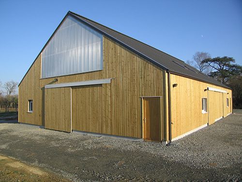 Grange en bois avec portes coulissantes et partie supérieure en tôle ondulée, posée sur du gravier.