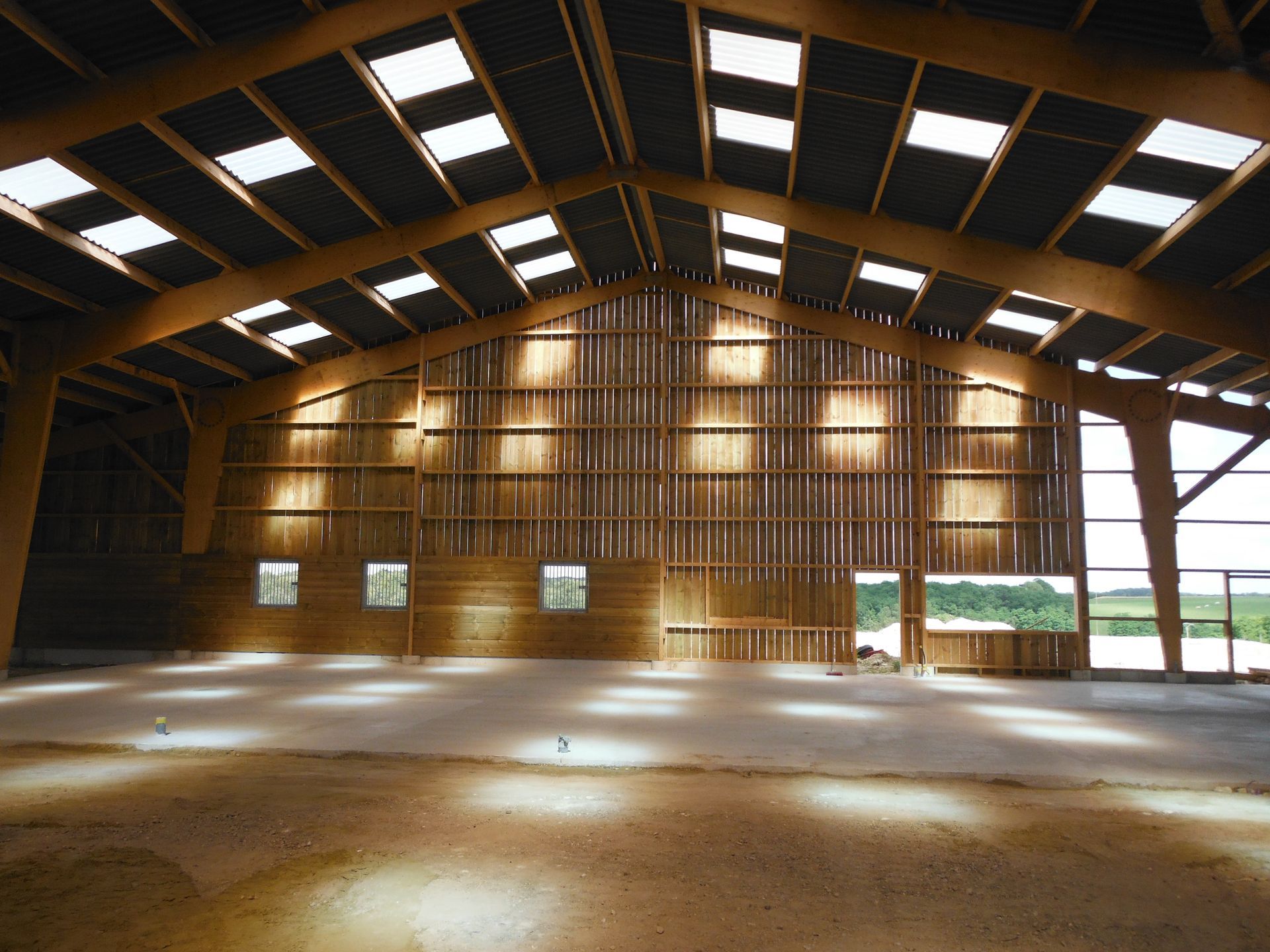 Intérieur d'une grande grange en bois où la lumière du soleil filtre à travers les panneaux du toit, sol en terre battue nu.