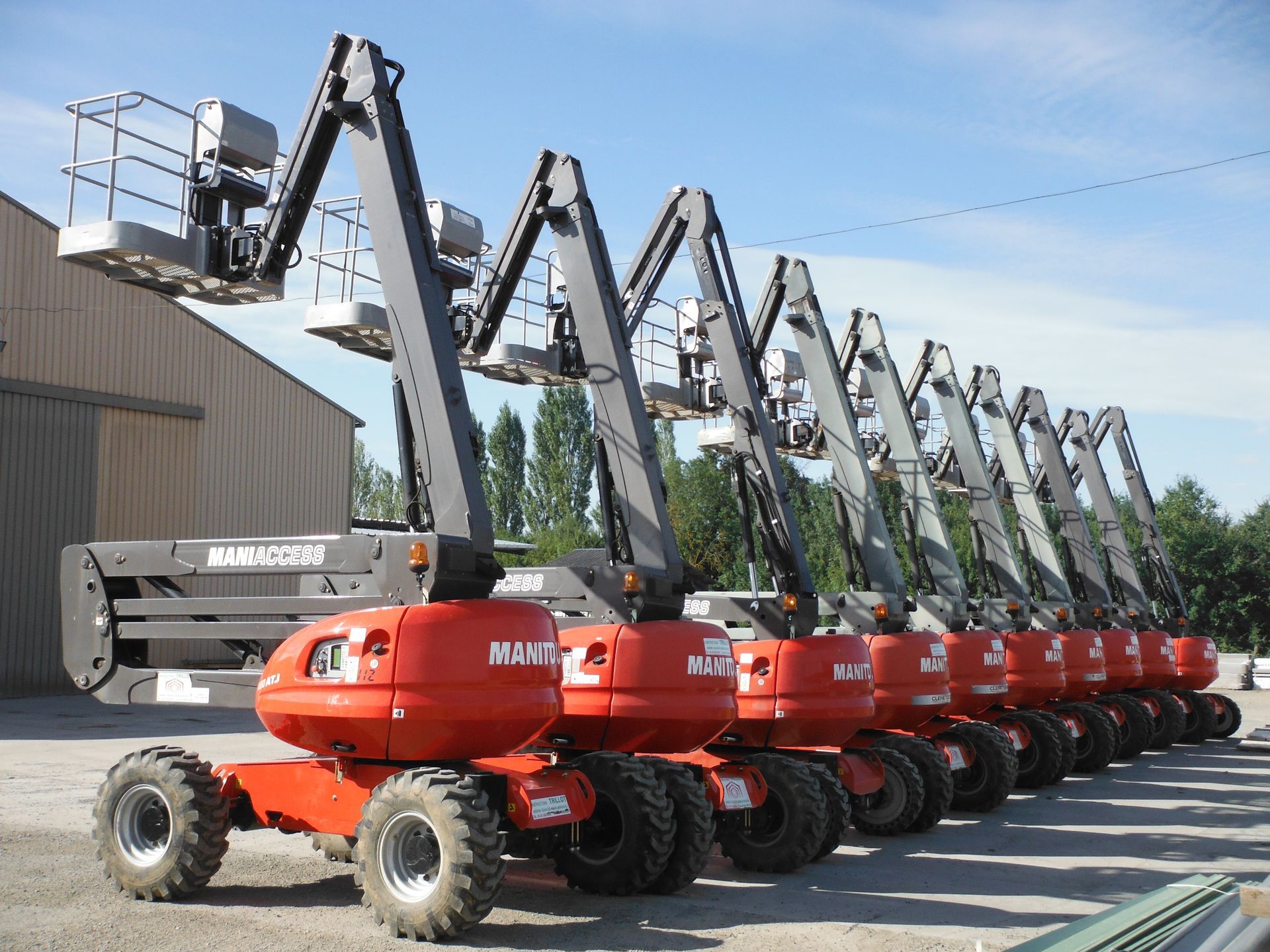 Rangée de nacelles élévatrices Manitou orange stationnées à l'extérieur.