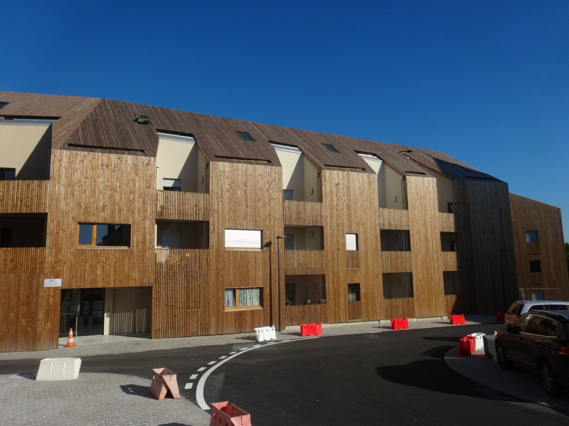 Bâtiment moderne avec bardage en bois et allée incurvée sous un ciel bleu azur.