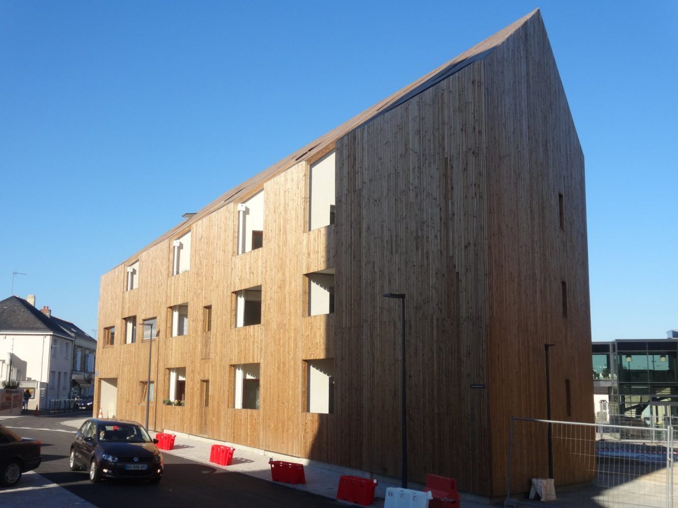 Bâtiment en bois aux fenêtres disposées de manière irrégulière, vue de rue, ciel bleu en arrière-plan.