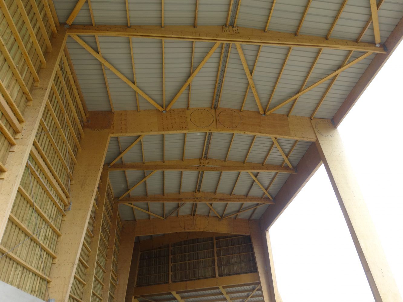 Vue intérieure de la charpente du toit d'un bâtiment en bois, avec panneaux métalliques et poutres de soutien.