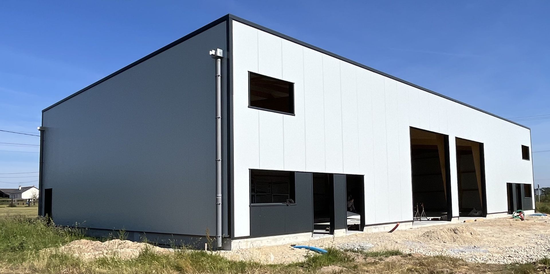 Un grand bâtiment industriel moderne, aux panneaux blancs et gris foncé, sous un ciel bleu.