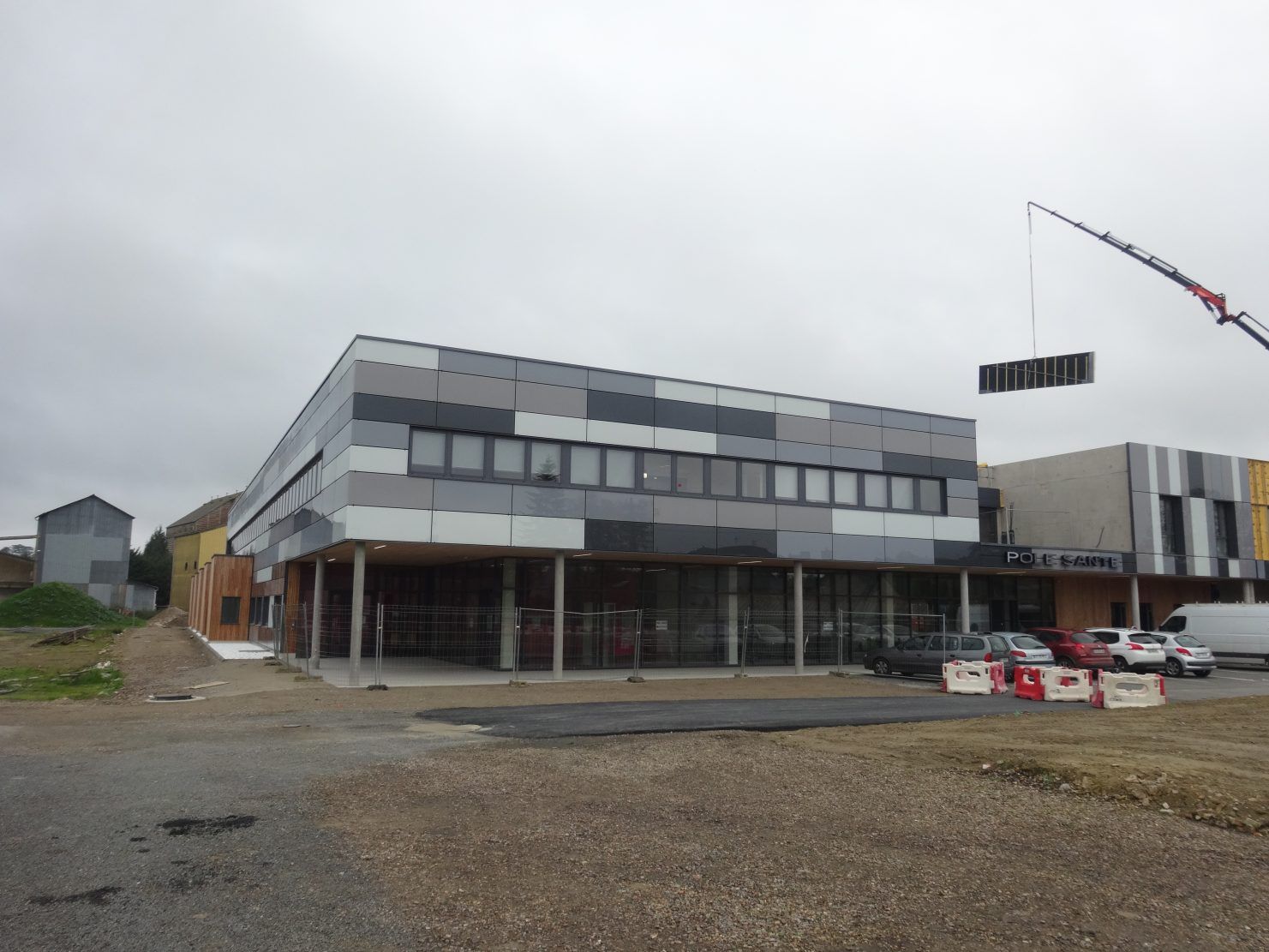 Bâtiment en construction avec façade grise, noire et blanche, grue en arrière-plan, ciel couvert.
