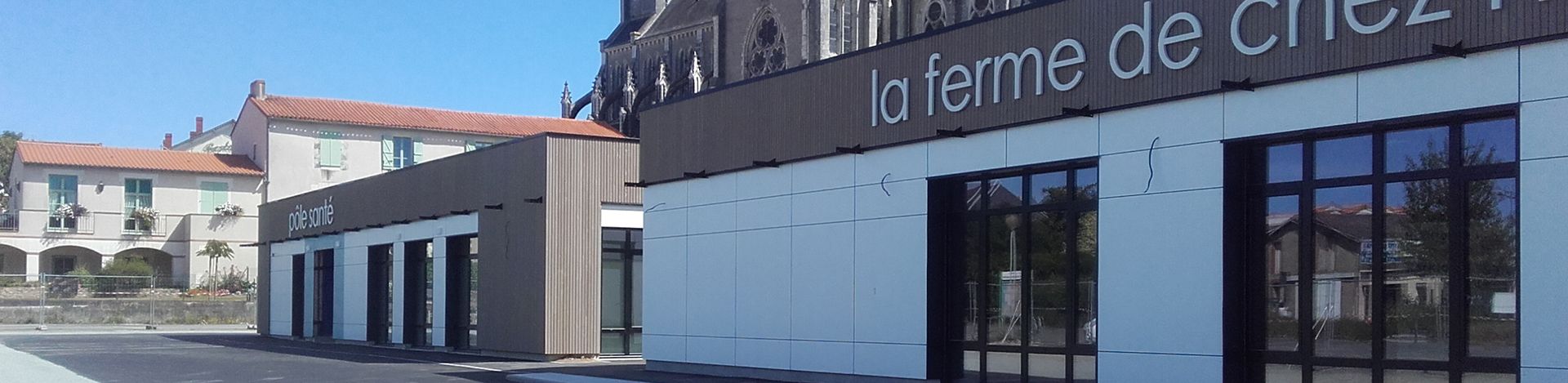 Un bâtiment moderne avec une enseigne indiquant « La ferme de Chez ». Le ciel bleu est visible.