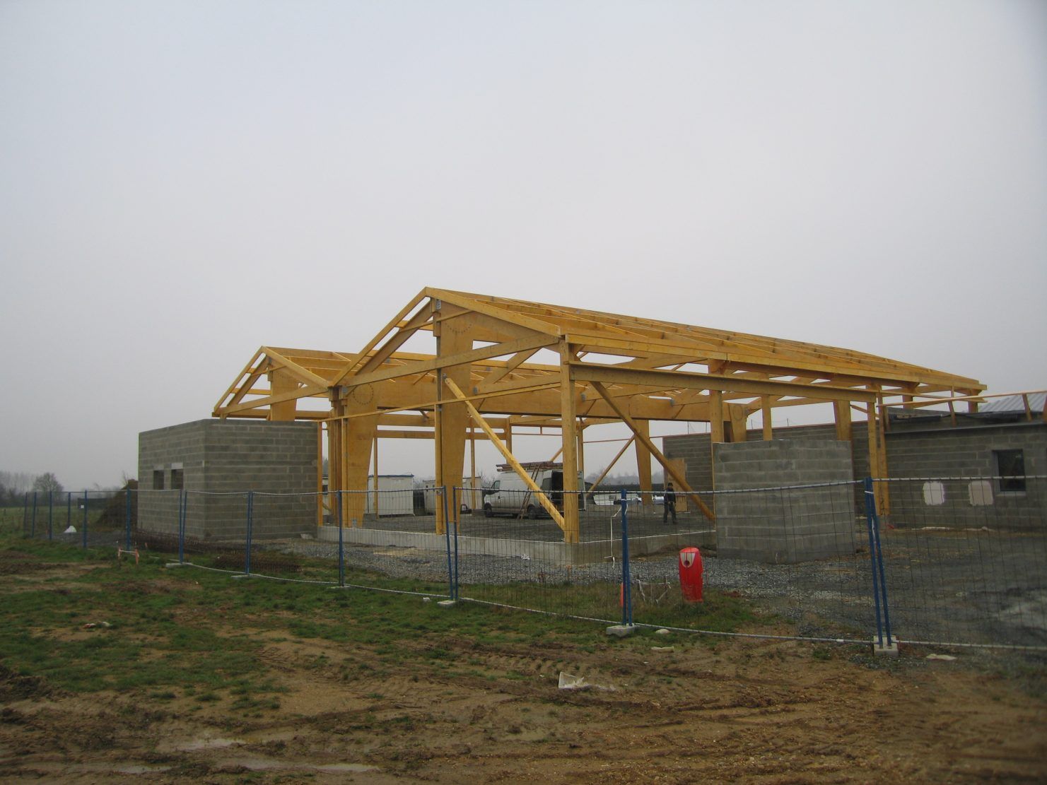 Structure à ossature bois en construction ; murs en parpaings gris, ciel couvert.