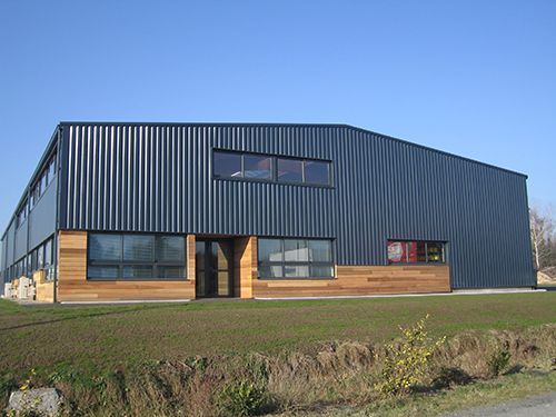 Bâtiment industriel moderne avec bardage en tôle ondulée, éléments en bois et petites fenêtres.