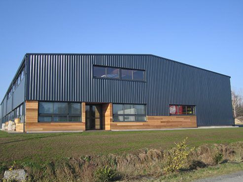 Bâtiment en tôle ondulée bleu foncé avec des éléments en bois, des fenêtres et de l'herbe verte.