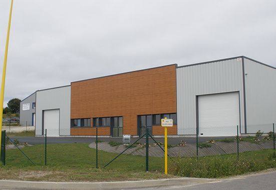 Bâtiment industriel moderne avec façade grise et brune, deux portes de chargement et cour clôturée.