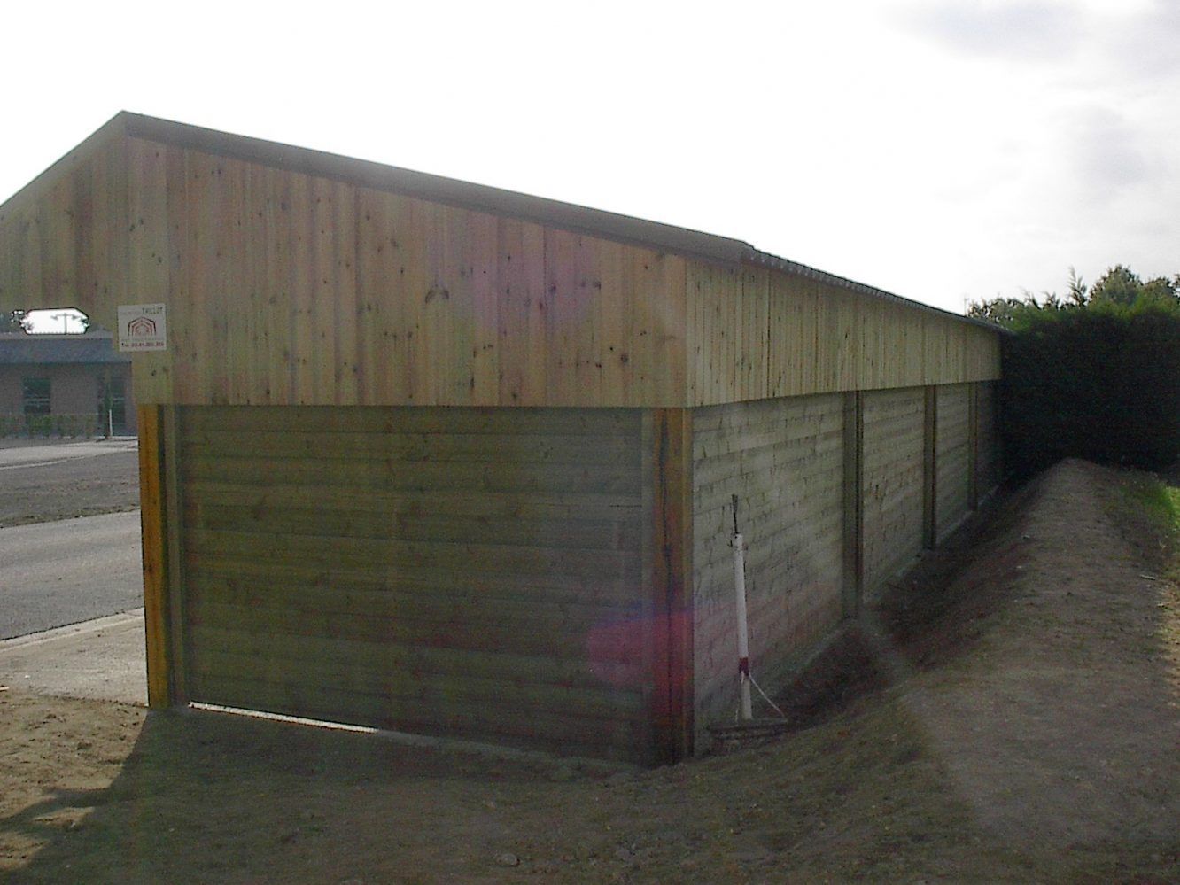 Abri en bois à toit en pente, intégré à un mur sur un chemin de gravier en bordure de route.