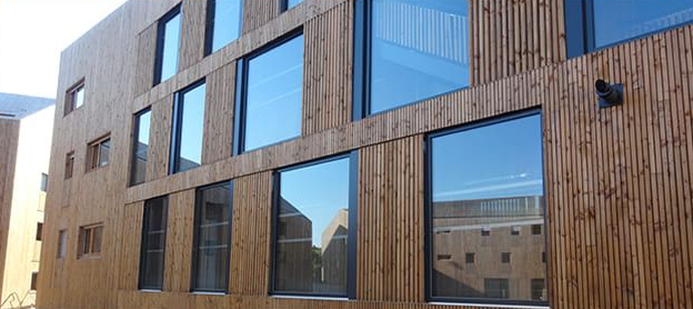 Bâtiment moderne avec façade en bois et grandes baies vitrées reflétant le ciel.