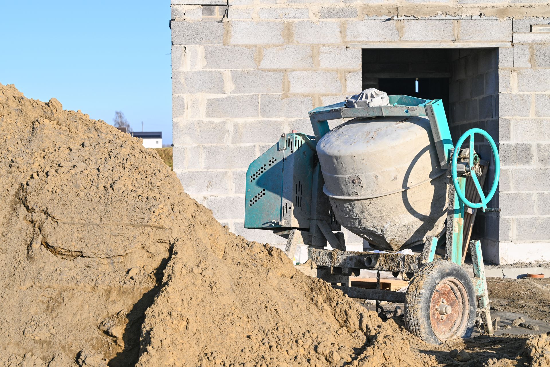 Une bétonnière et un tas de sable devant une maison en construction