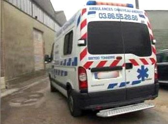 Une ambulance aux couleurs rouge et bleue est garée dans une ruelle étroite.