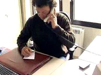 Une personne assise à un bureau, parlant au téléphone et écrivant sur un bloc-notes dans un bureau lumineux.
