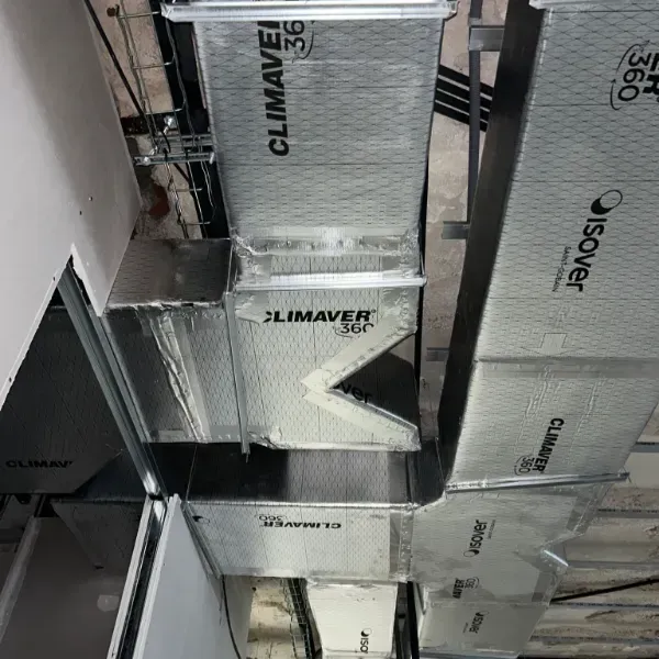 Instalación de conductos HVAC en un edificio comercial con conductos de plata aislados y soportes de techo.