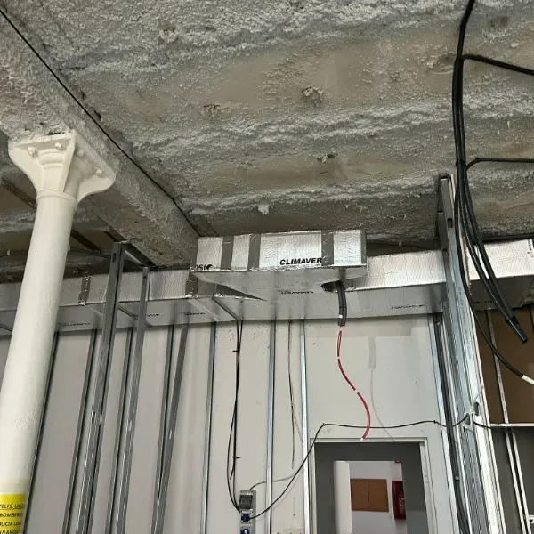 Interior del sitio de construcción que muestra el techo expuesto, la estructura de metal y los cables eléctricos.