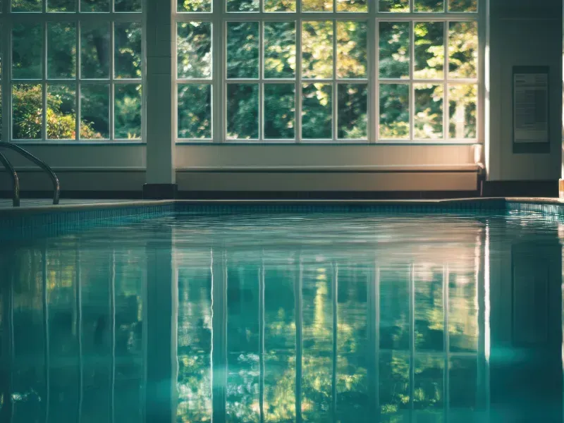 Piscina cubierta con reflejos de ventanas y árboles.