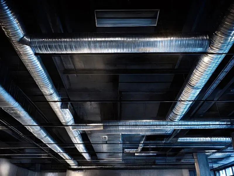 Conductos de ventilación plateados contra un techo oscuro.