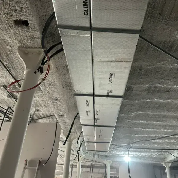 Conductos aislados instalados sobre un techo de hormigón, con columnas de soporte y cableado eléctrico visibles.