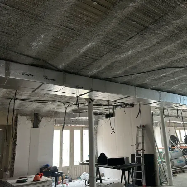 Espacio interior en construcción, con conductos de techo, cableado eléctrico y columnas de soporte.