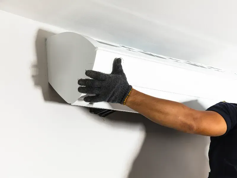 Persona instalando una unidad de aire acondicionado blanca en una pared blanca.