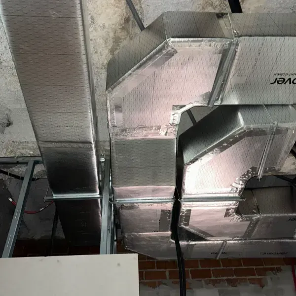 Conductos metálicos de HVAC instalados cerca de un techo de hormigón, sostenidos por una estructura de metal.