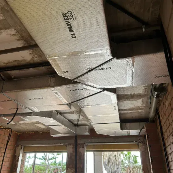 Conductos HVAC aislados instalados en un techo de concreto, sujetos en su lugar con correas negras.