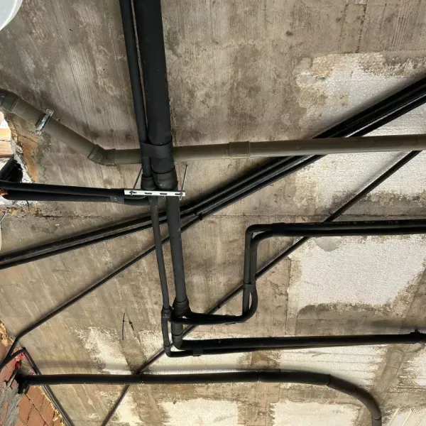 Tubos negros de distintos tamaños que recorren un techo de hormigón.