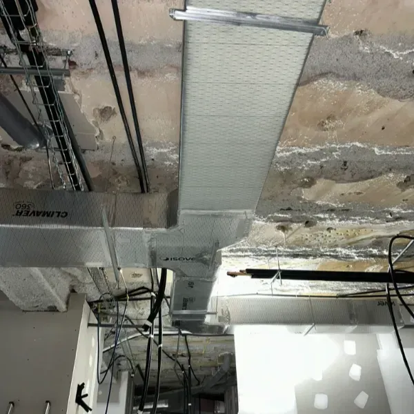 Vista aérea de una construcción sin terminar, con conductos, cables y un techo parcial visibles.