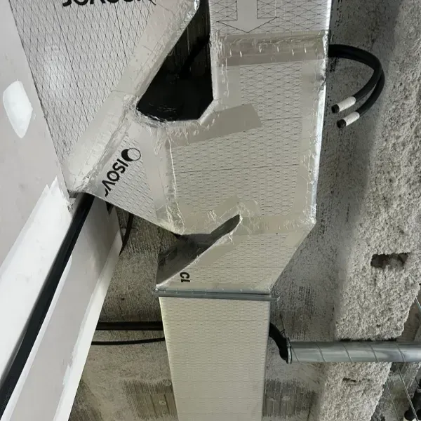 Conductos HVAC aislados, plateados con tubos negros, instalados en un techo de hormigón.