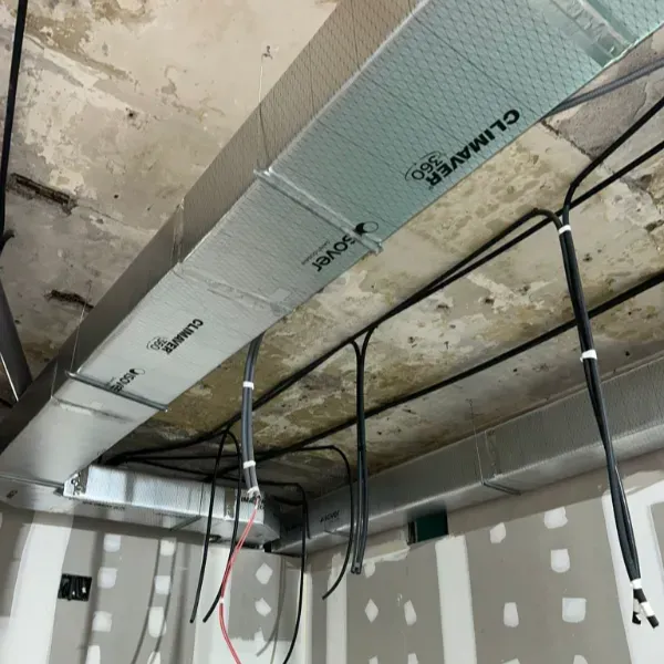 Conductos de aire acondicionado y cableado eléctrico instalados en un techo de hormigón. El aislamiento indica 