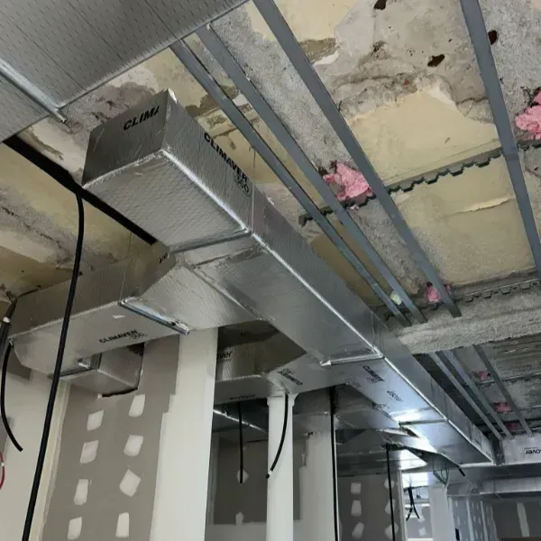 Instalación de conductos HVAC en un edificio en construcción; conductos con aislamiento de plata contra un techo de hormigón.
