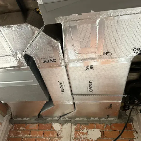 Conductos aislados sobre una pared de ladrillos, cubiertos con cinta adhesiva plateada.