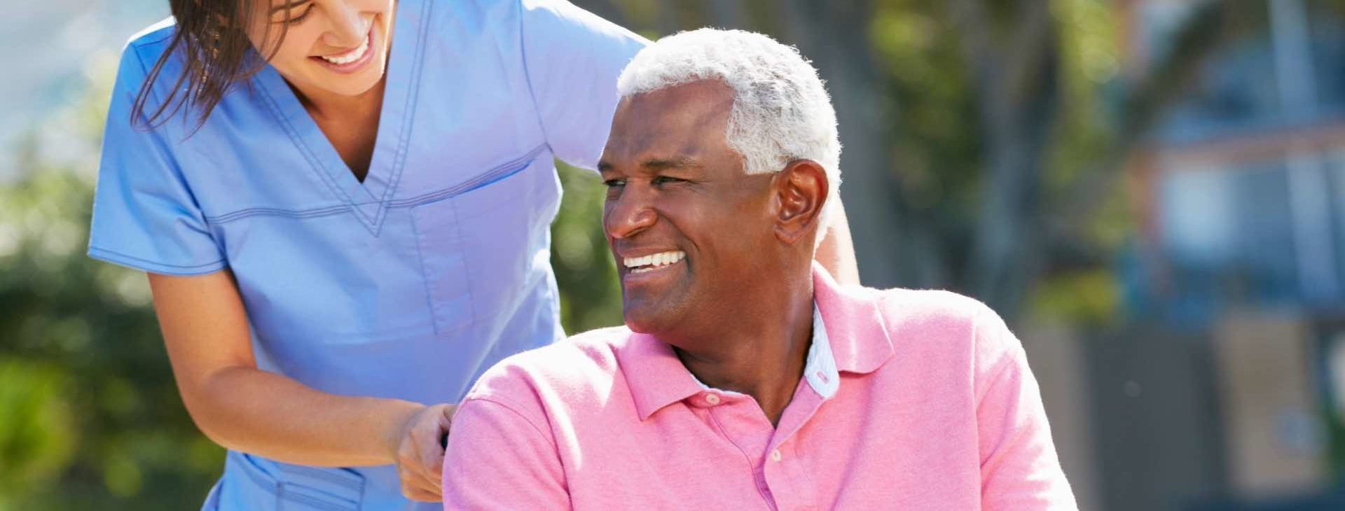 Une personne en blouse médicale aide une personne souriante vêtue d'une chemise rose à l'extérieur.