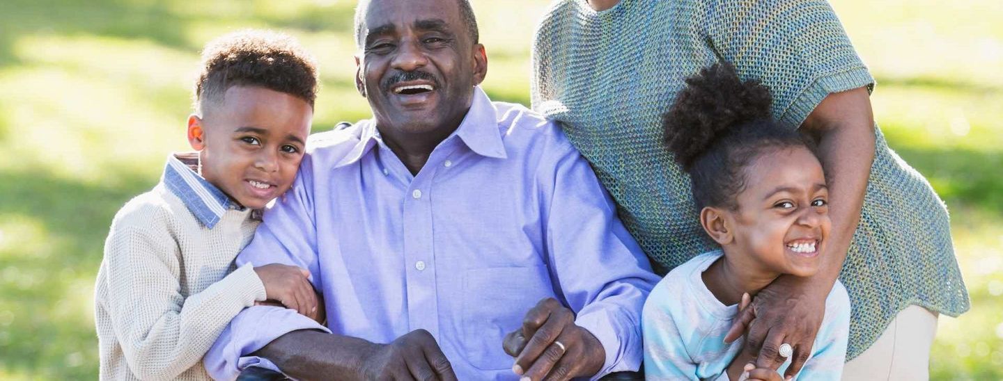 Une famille souriant ensemble à l'extérieur ; un garçon, une fille et un couple de personnes âgées.