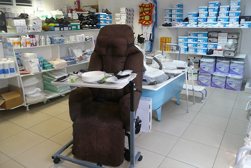 Un magasin de fournitures médicales avec un fauteuil inclinable marron sur lequel repose un plateau d'ustensiles, une baignoire et des étagères remplies de matériel.