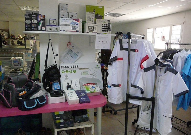 Magasin de fournitures médicales avec des étagères remplies d'équipements, des blouses blanches de laboratoire sur un portant et des sacs sur une table.