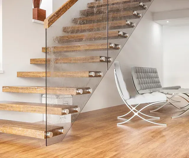 Una escalera de madera con barandilla de cristal en una sala de estar.