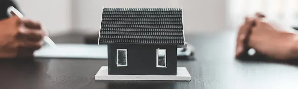 Una casa modelo está sobre una mesa al lado de una persona que escribe en un trozo de papel.
