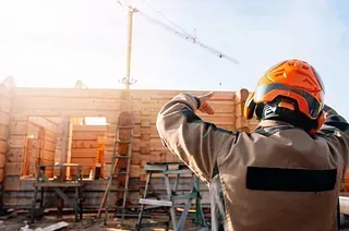 Un trabajador de la construcción está parado frente a una casa de madera en construcción.