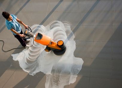 Una mujer está limpiando un piso de baldosas con una máquina.