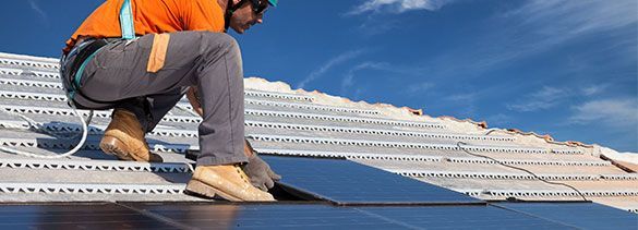 Un hombre está arrodillado sobre un tejado instalando paneles solares.
