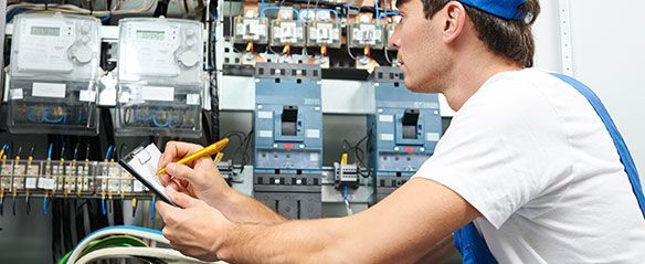 Un hombre está trabajando en un panel eléctrico y escribiendo en un portapapeles.