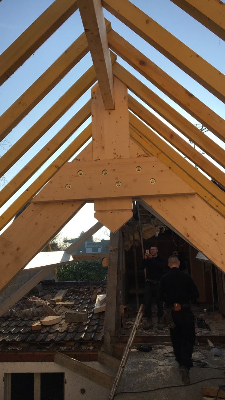 Charpente de toit en bois en construction, ouvriers debout sur le toit en contrebas, ciel bleu.