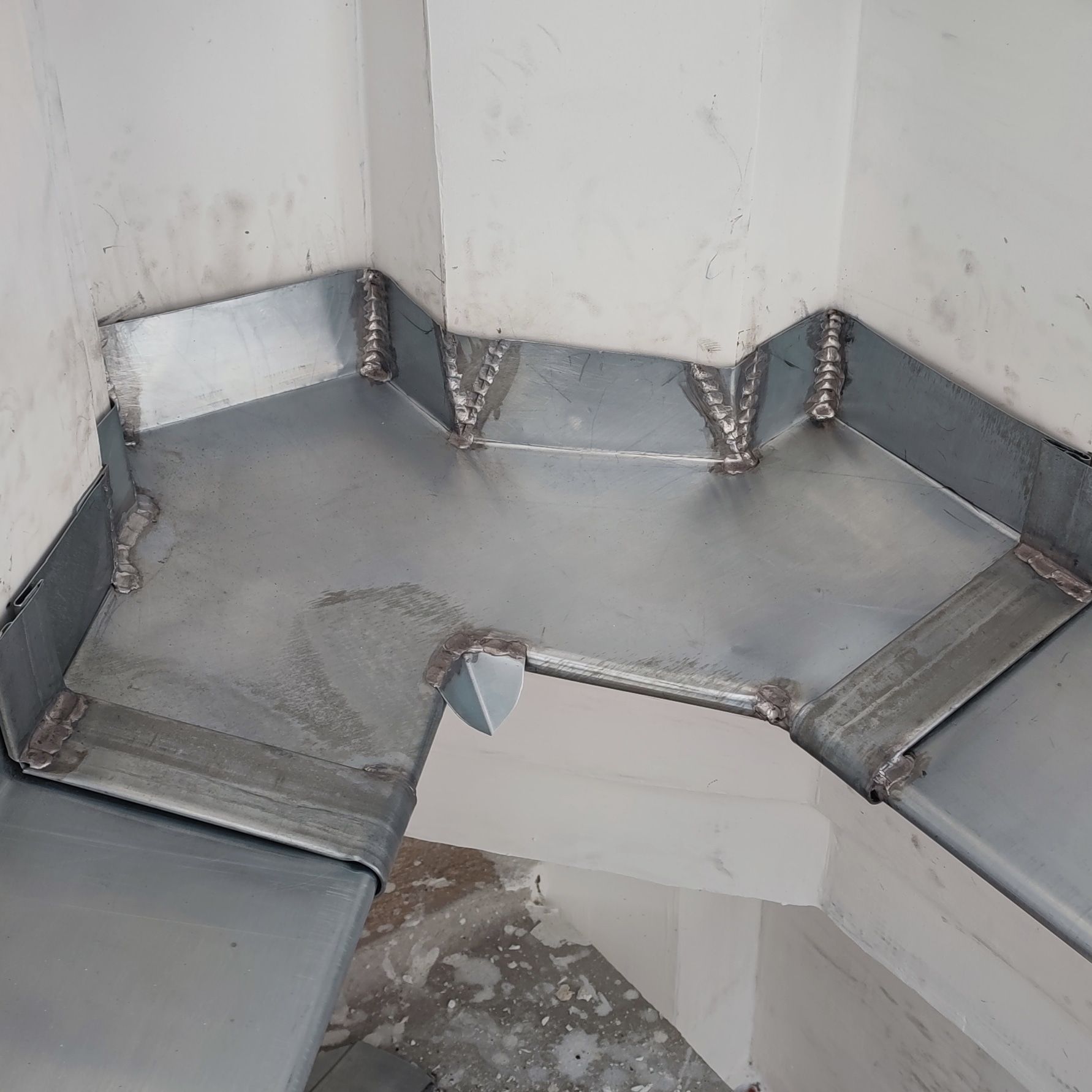 Conduits métalliques installés dans un coin, avec soudures apparentes et couleur grise.